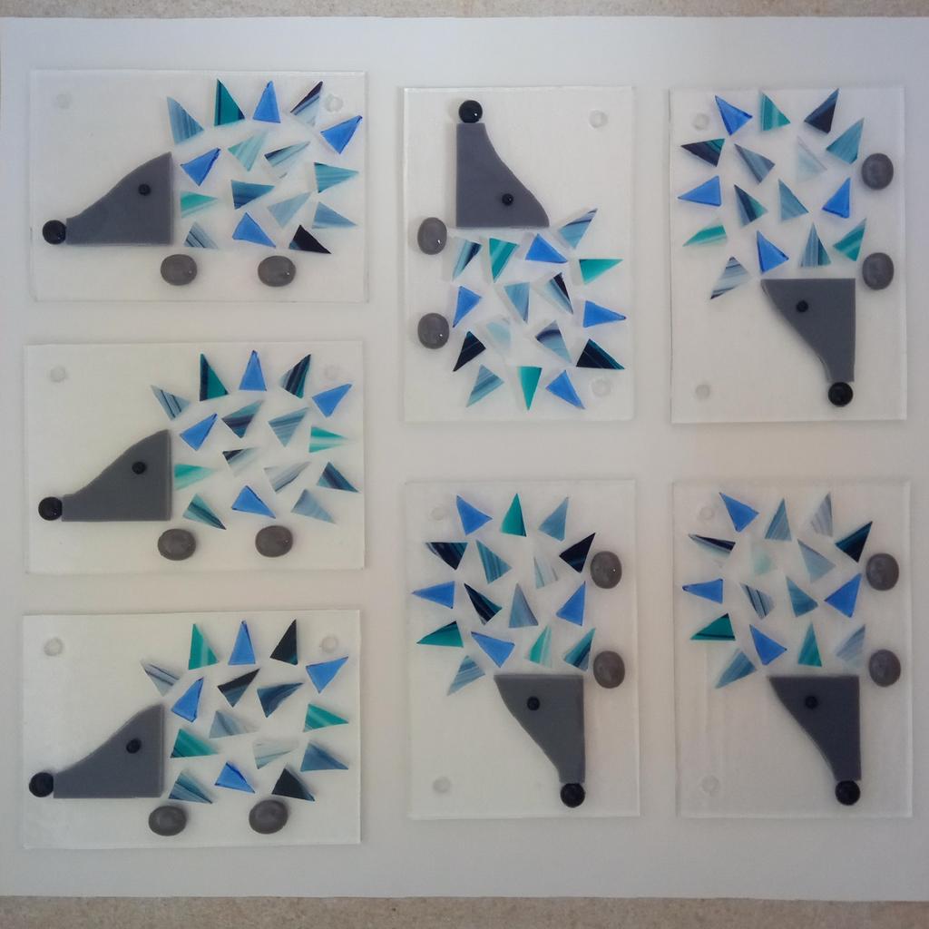 Photo of seven blue hedgehog wall hangings, arranged on the kiln shelf ready to be fused