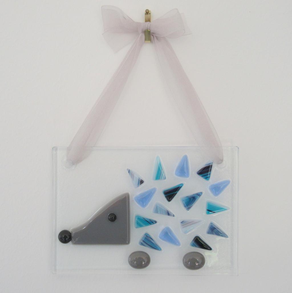 Photo of a fused glass hedgehog wall hanging with blue prickles, hung on a white wall